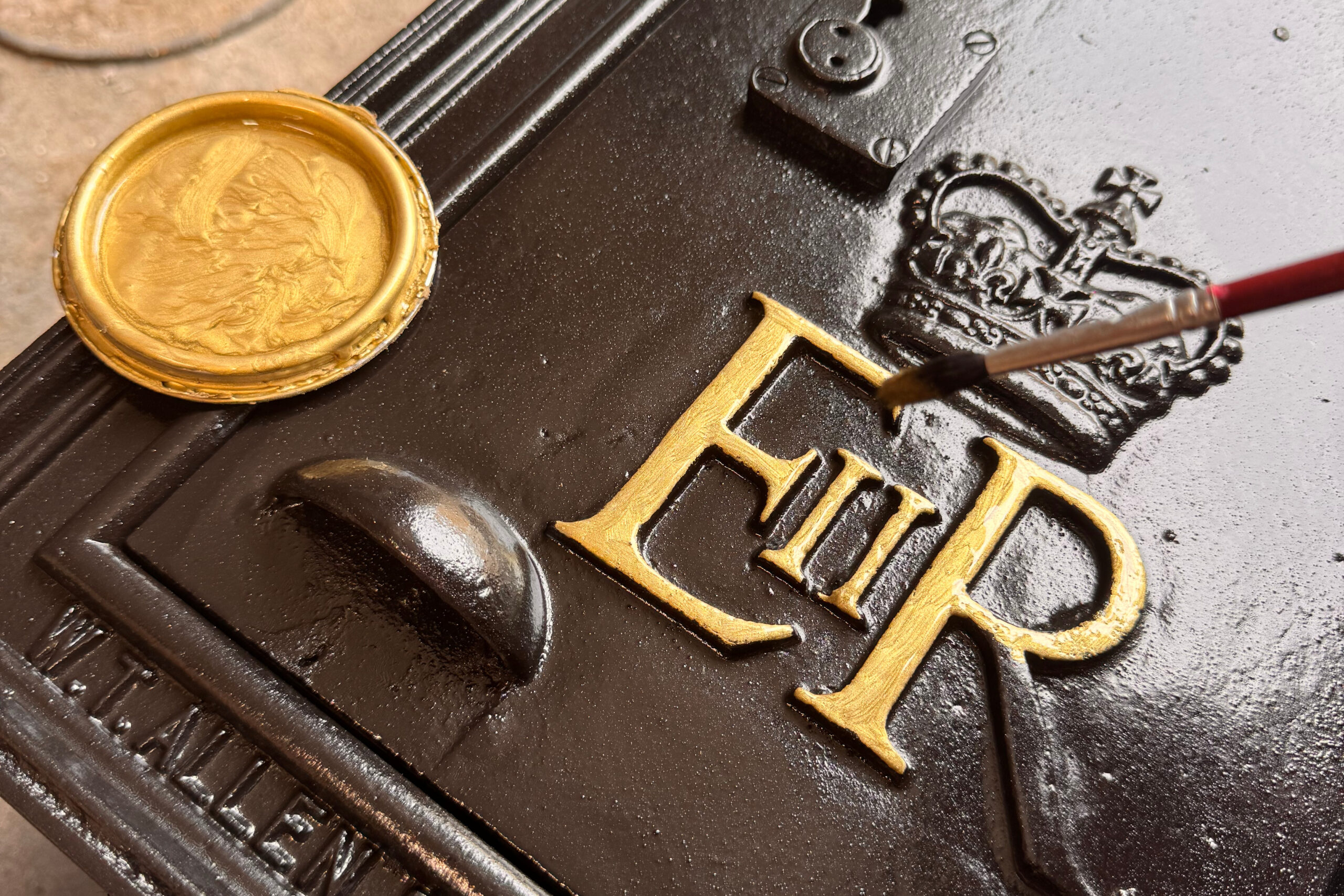 Hand painting gold detail onto the EIIR royal cypher of a cast iron post box